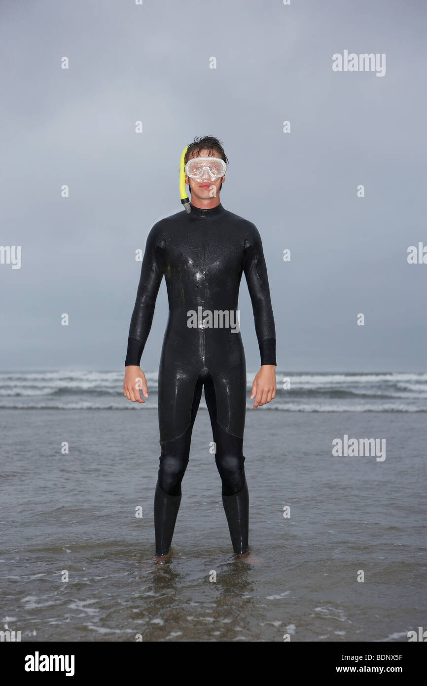 Man in wetsuit wearing snorkle, standing in water on beach, portrait