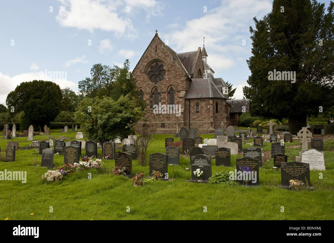Gable end of a rural village stone-walled church as seen across the headstones in the graveyard on a blue skied summers day Stock Photo