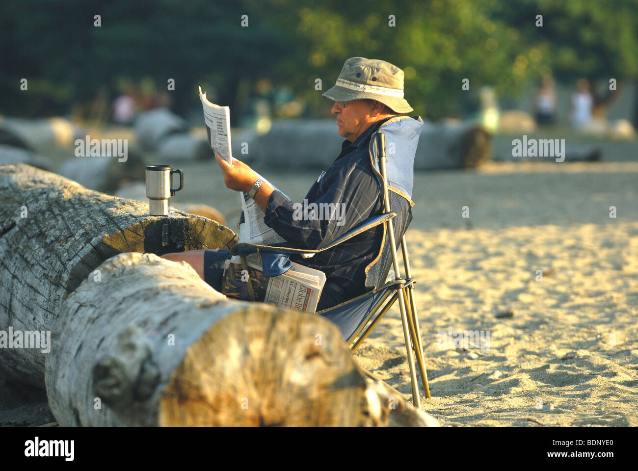 Man sitting at a Vancouver beach enjoying reading the early morning paper and a coffee. Stock Photo