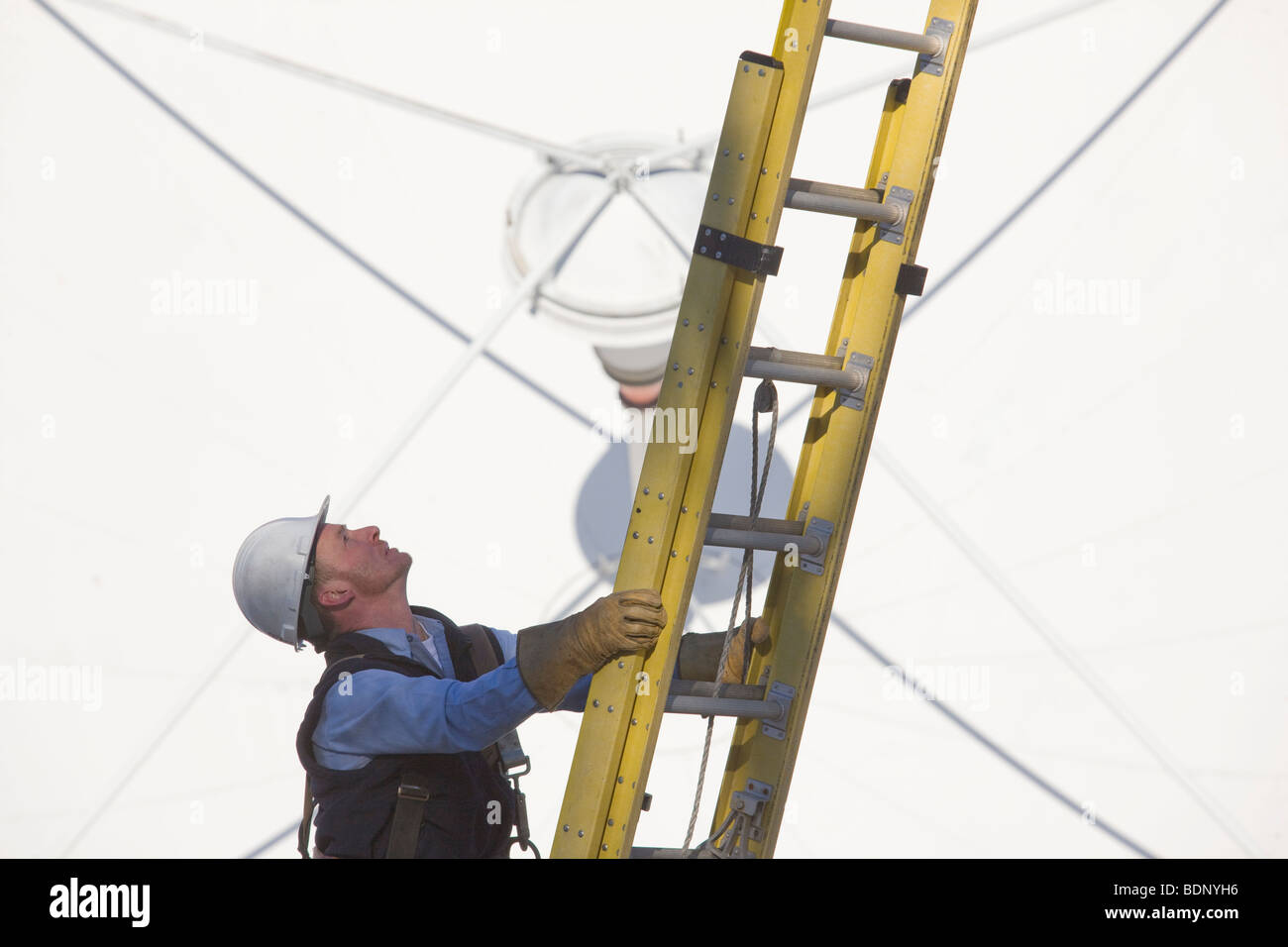 Cable lineman climbing a ladder in front of a satellite dish Stock Photo