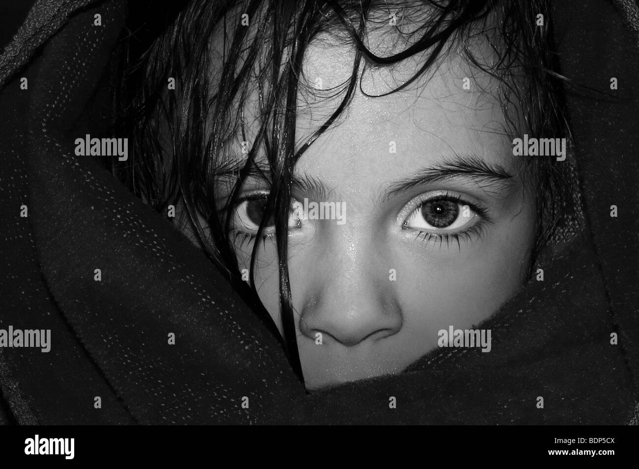 Black and white image of a young female child wrapped in a blanket looking out with large eyes and wet hair.. Stock Photo