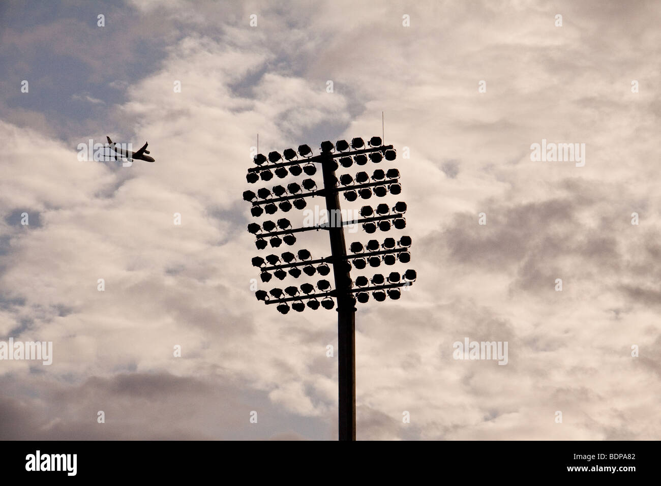 Airplane flying over stadium lights, London, UK Stock Photo