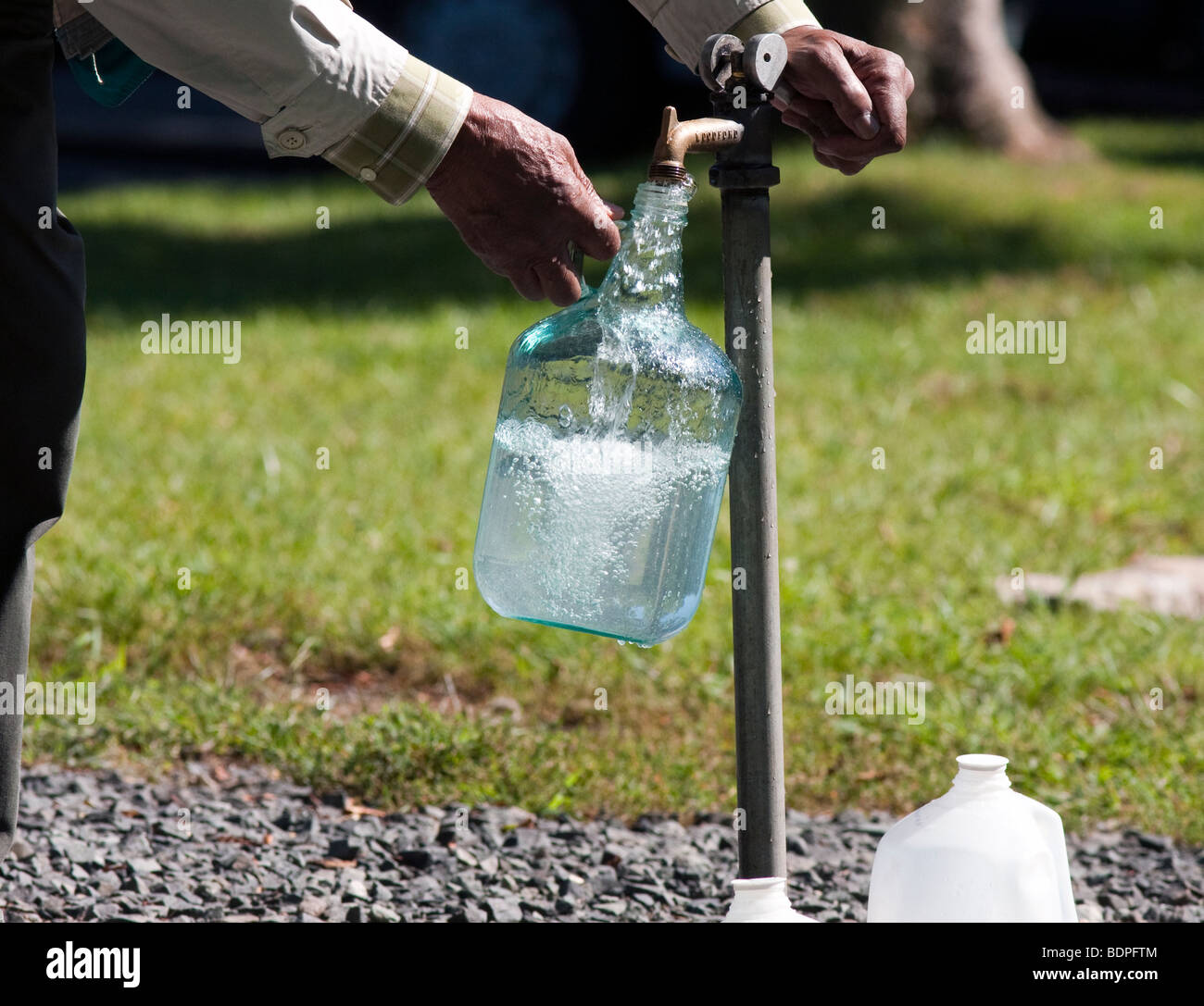 Filling a large glass jug at an outdoor tap with pure clean well water