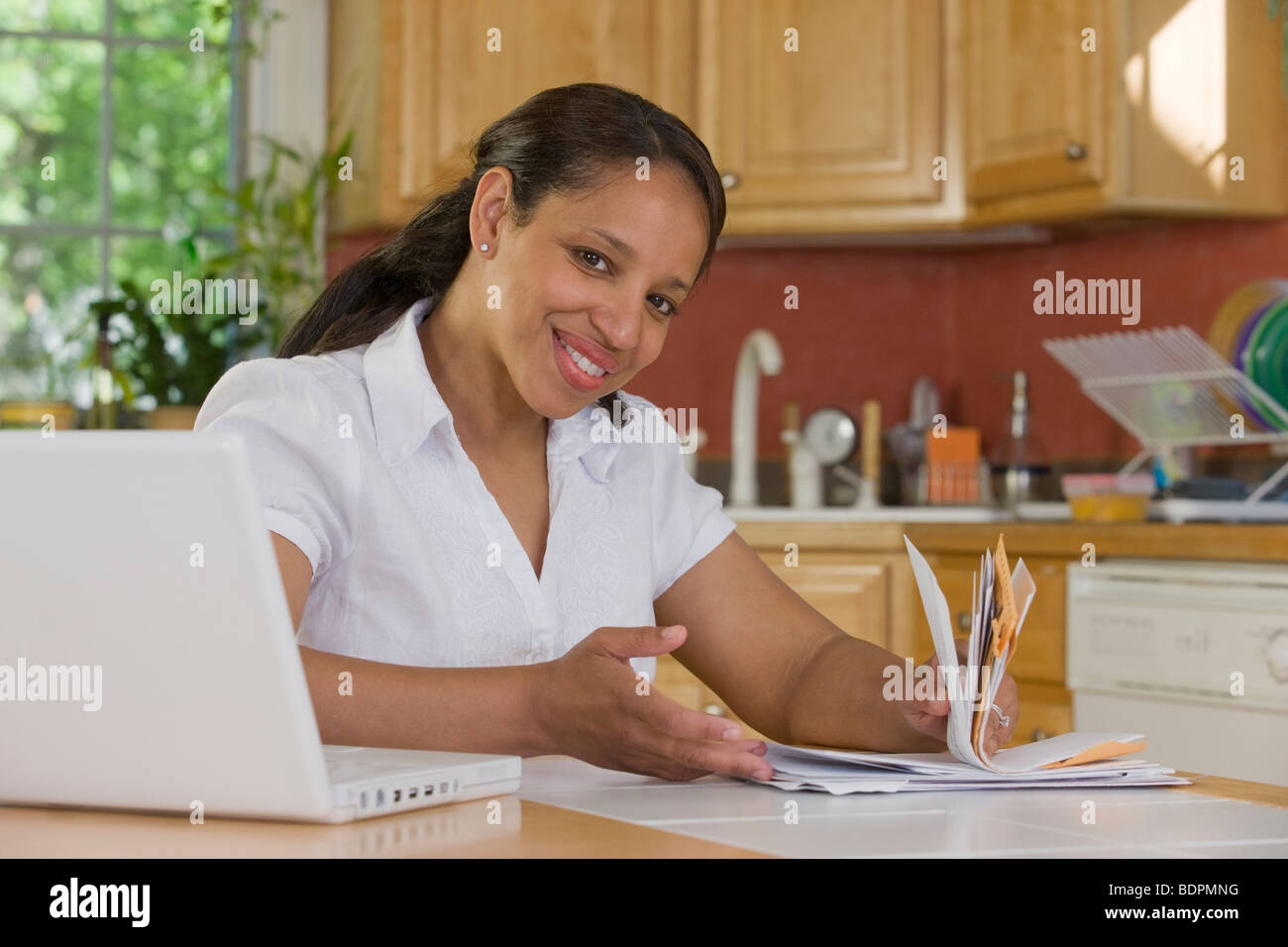 Hispanic woman sitting in front of a laptop and holding bills in the kitchen Stock Photo