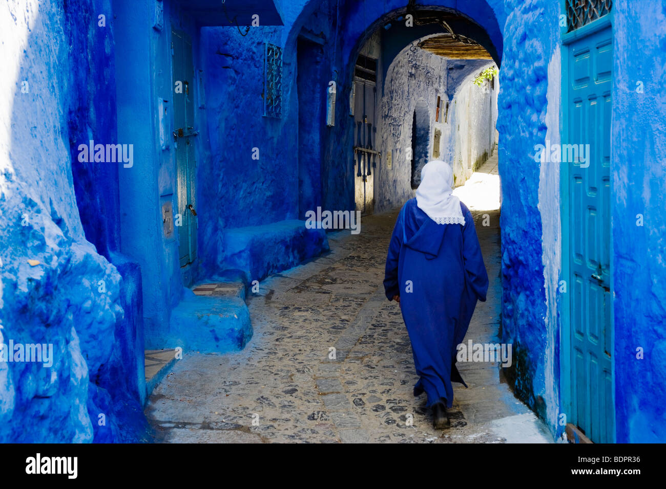 Chefchaouen, woman in blue jalaba and traditional blue-painted doors and walls in the old town. Stock Photo