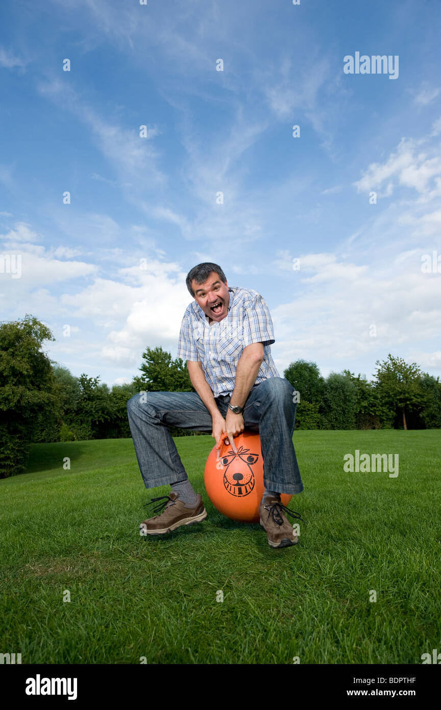 Grown man bouncing on a space hopper during summer in England Stock Photo