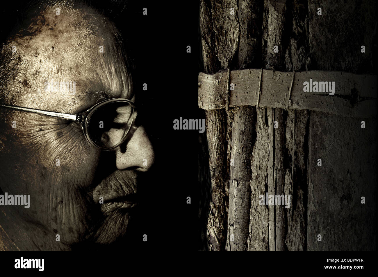 The profile of an old woman wearing glasses standing next to wattle and daub Stock Photo