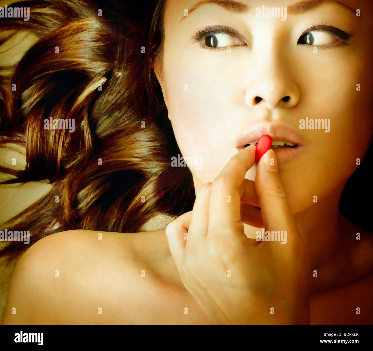 Close up of a young asian womans face placing a red pill to her lips Stock Photo