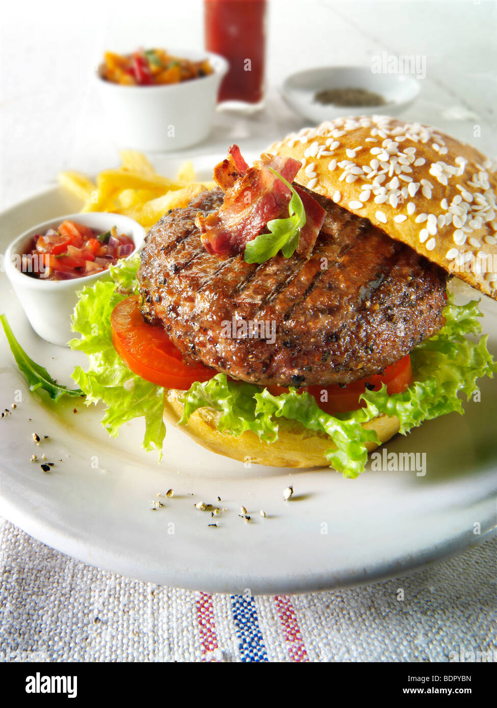Char grilled beef burger and bacon with chips and salad and a seseme bun Stock Photo