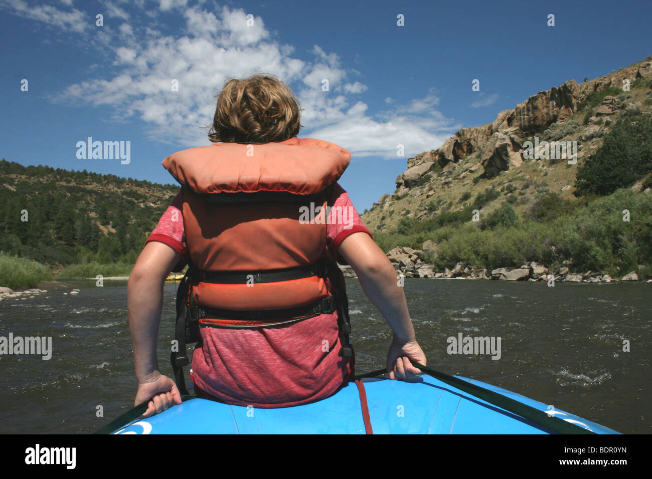 ten year old boy wearing life jacket sits in the front of an inflatable boat, river ride in Colorado Stock Photo