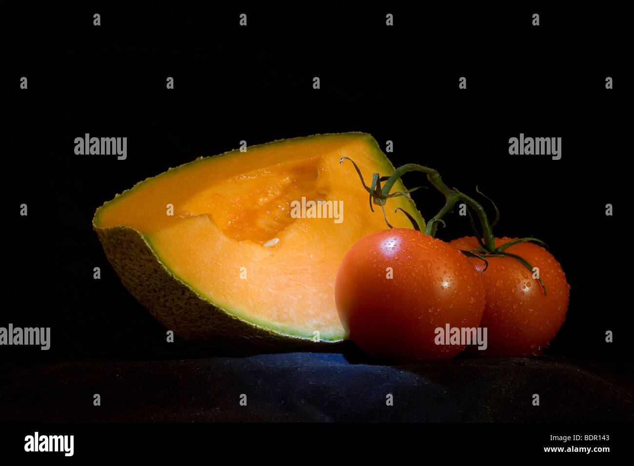 Still life with melon and tomato against black background Stock Photo