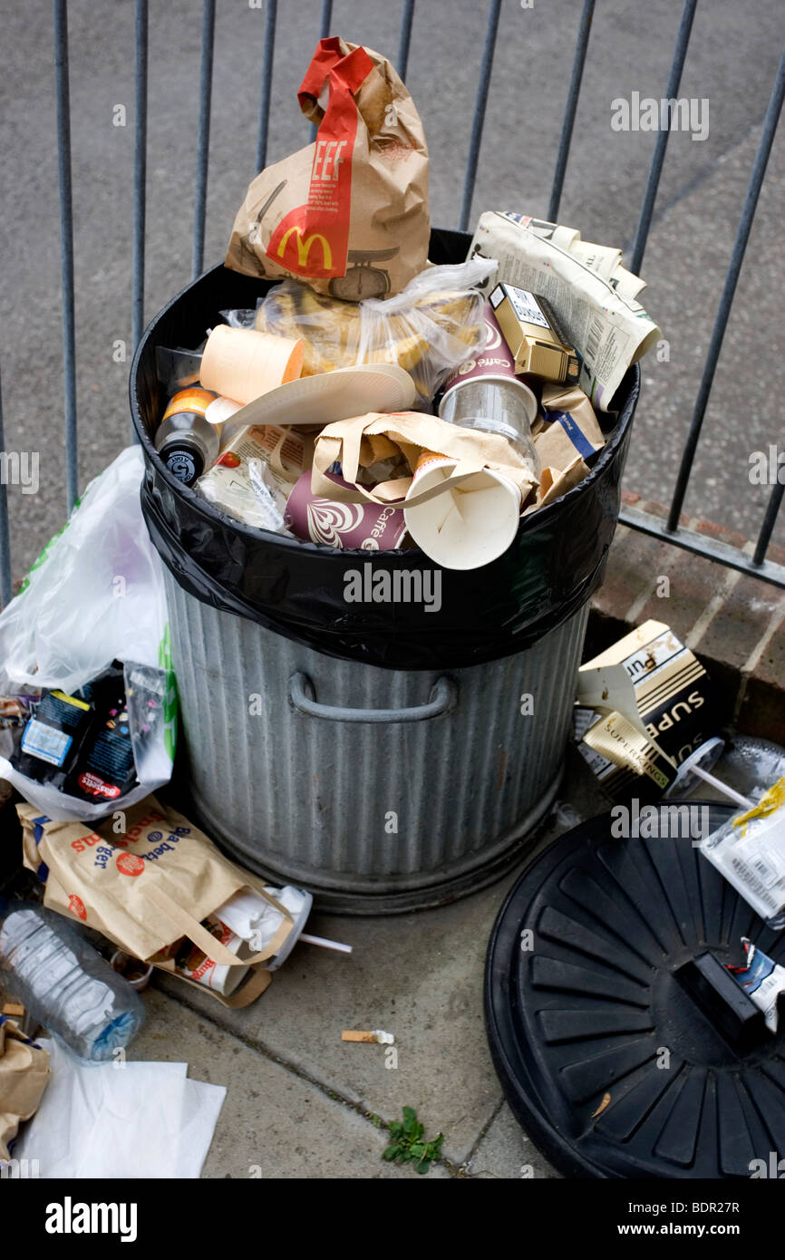 An overflowing silver metal bin filled with overflowing waste and rubbish in in Brighton, East Sussex, UK. Stock Photo