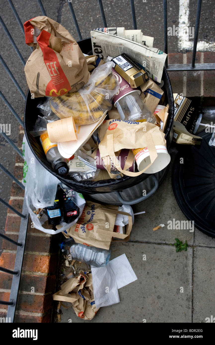 An overflowing silver metal bin filled with overflowing waste and rubbish in in Brighton, East Sussex, UK. Stock Photo