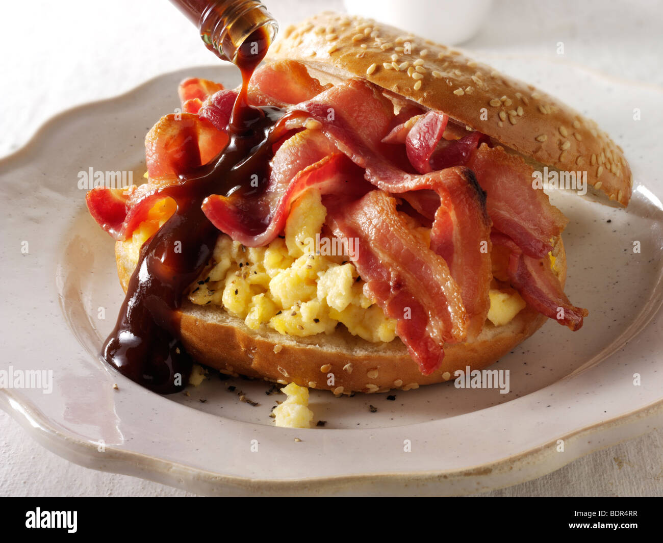 Crispy streaky bacon and scrambled eggs on a bagel with brown sauce Stock Photo