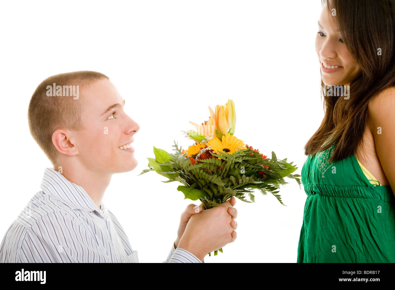 Junger Mann kniet mit Blumen vor seiner Freundin nieder, um ihr einen Antrag zu machen Stock Photo