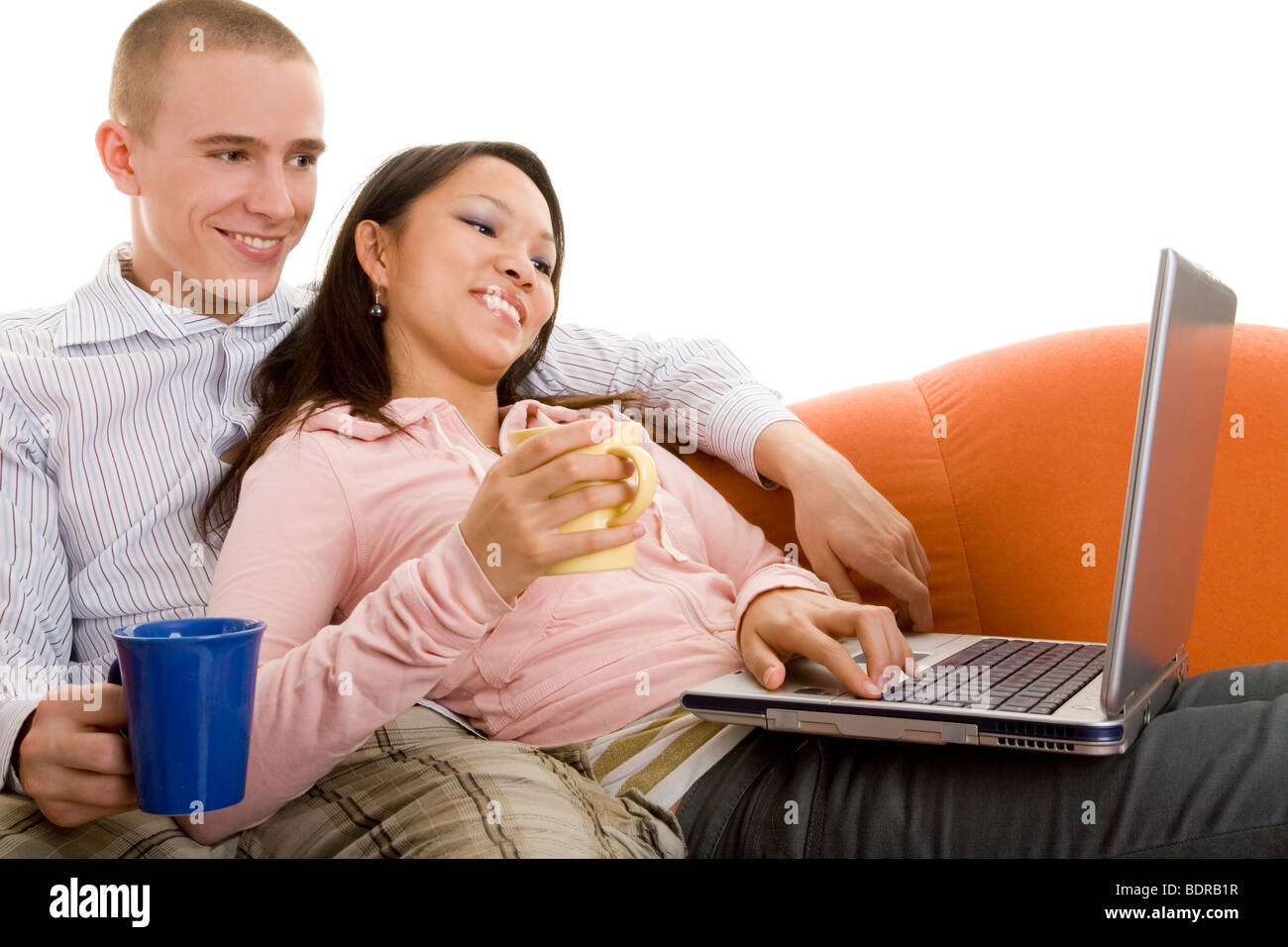 Junges Paar sitzt lachend auf dem Sofa mit Teetassen und Laptop Stock Photo