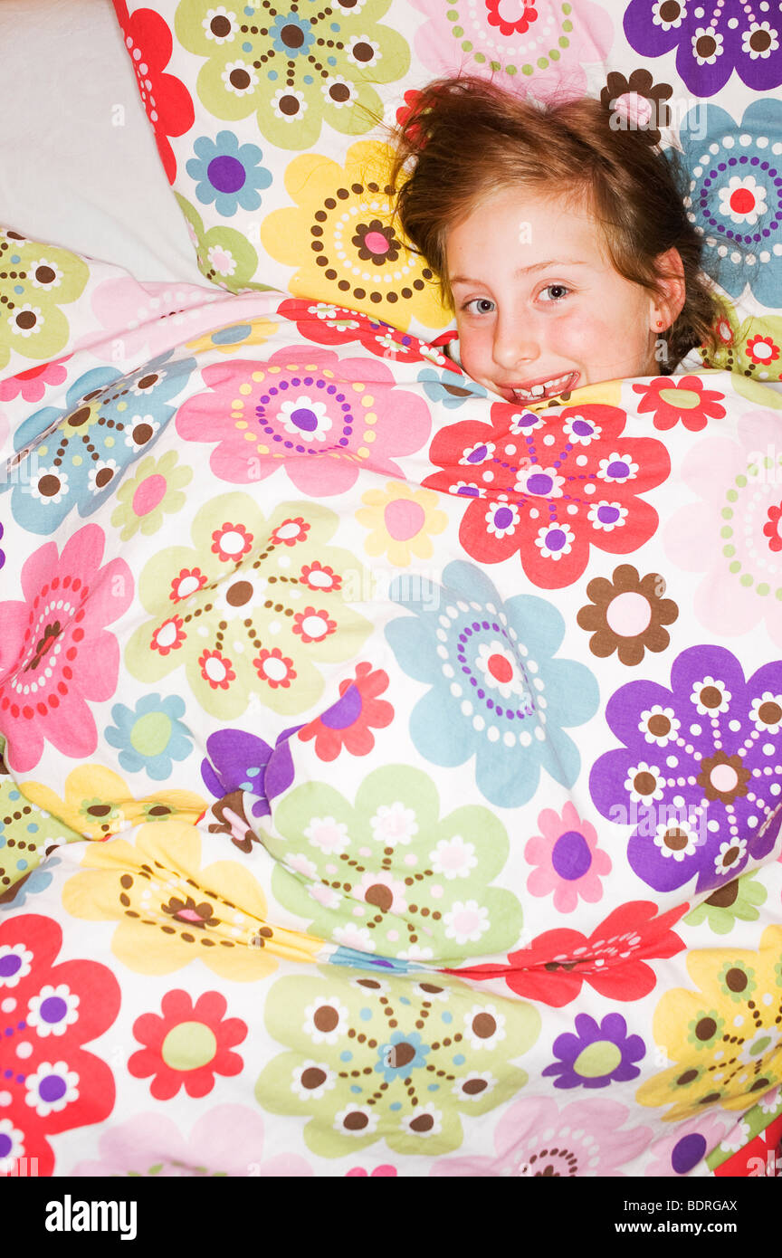 A happy girl lying under a flowery quilt Stock Photo