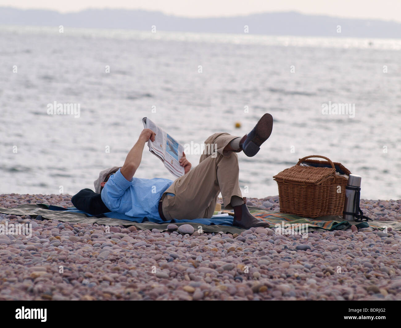 Man laid on the beach reading the paper. Stock Photo