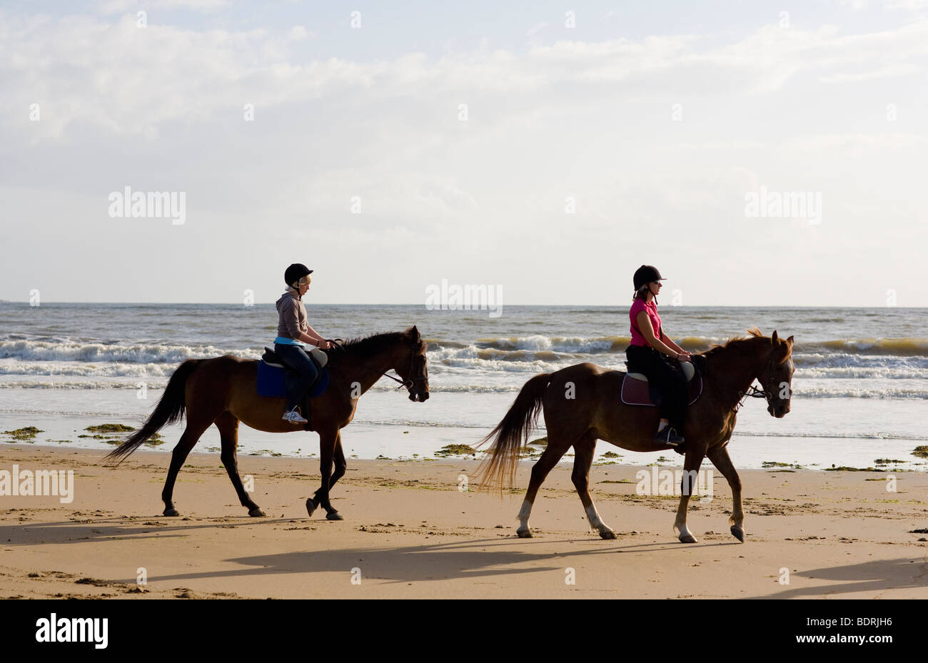 A horse riding school goes for a hack on the beach and in the surf. Riders are of all different ages and abilities. Stock Photo