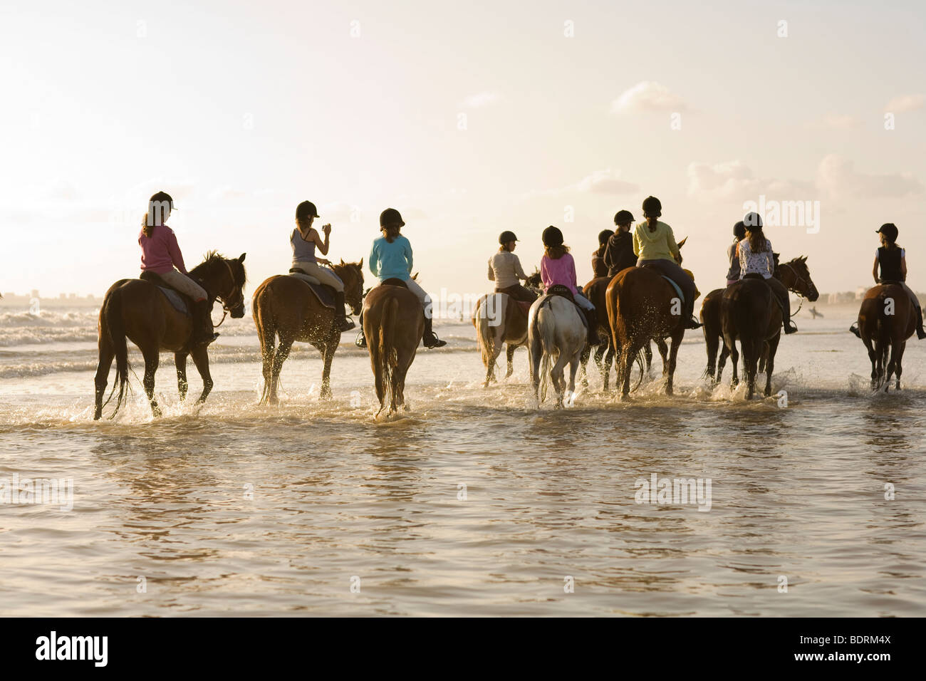 A horse riding school goes for a hack on the beach and in the surf. Riders are of all different ages and abilities. Stock Photo