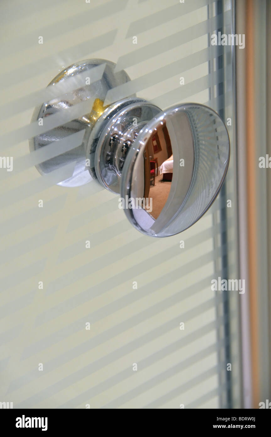 Door handle to an en suit shower cubicle with a reflection of a corner of the bedroom on it. Stock Photo