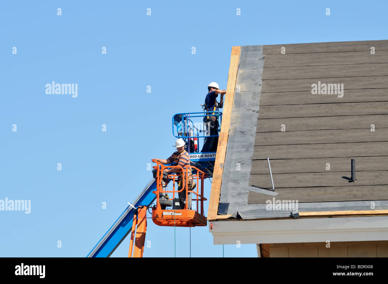 2 construction workers in aerial lifts working on exterior of new building Stock Photo