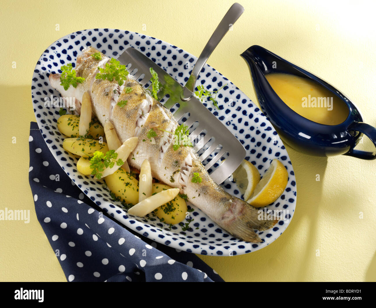 Pike perch with asparagus, potato, lemon, parsley and Riesling sauce in a gravy boat, blue dotted napkin Stock Photo