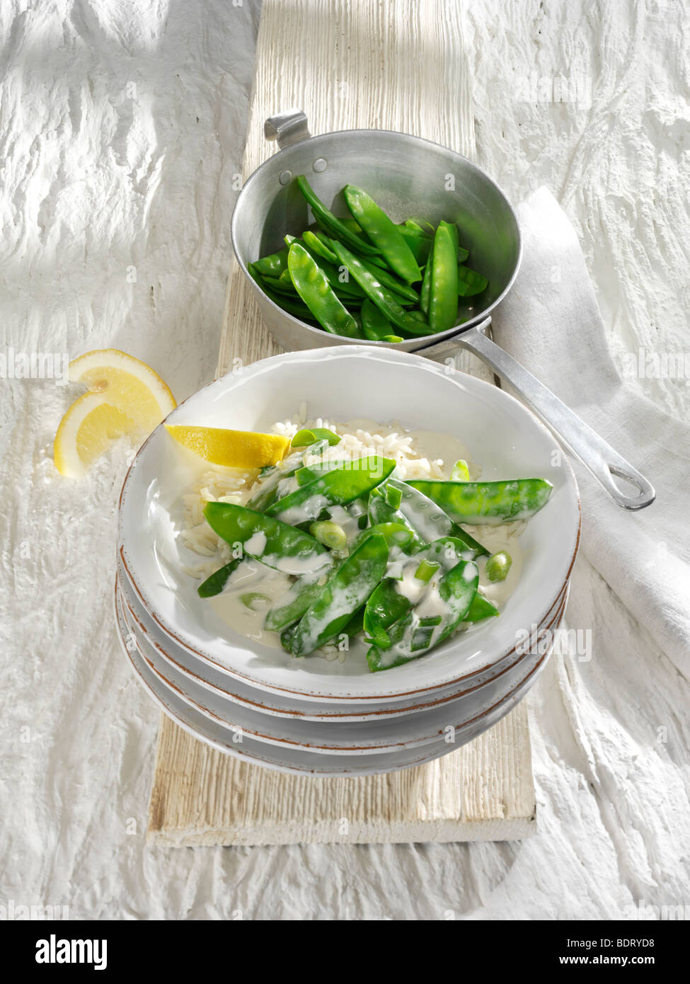 Snow peas with lemon sauce and lemon slices for squeezing in a stack of earthenware dishes Stock Photo