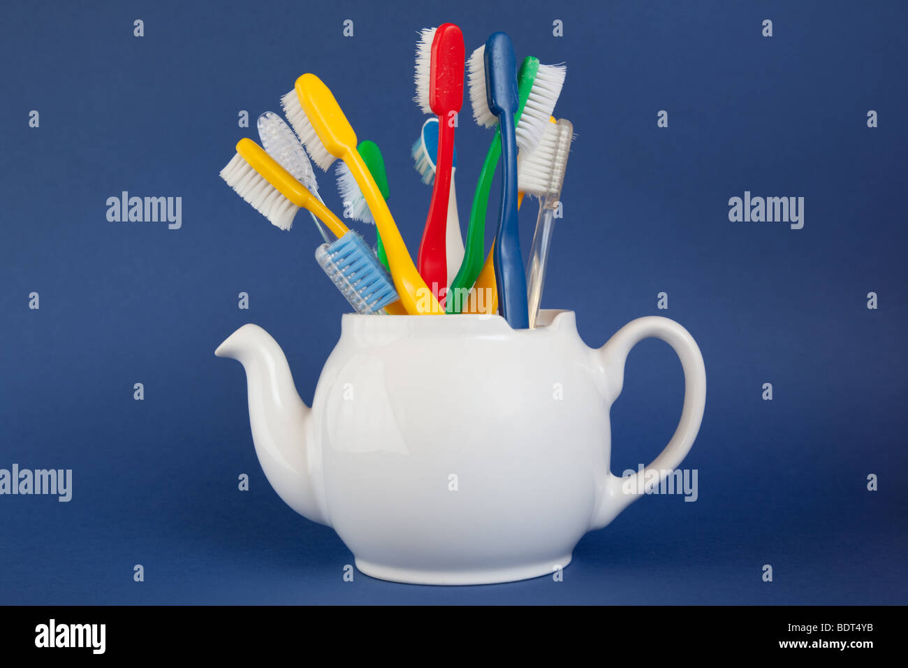 Old toothbrushes of varied colors in a small white teapot with a blue background Stock Photo