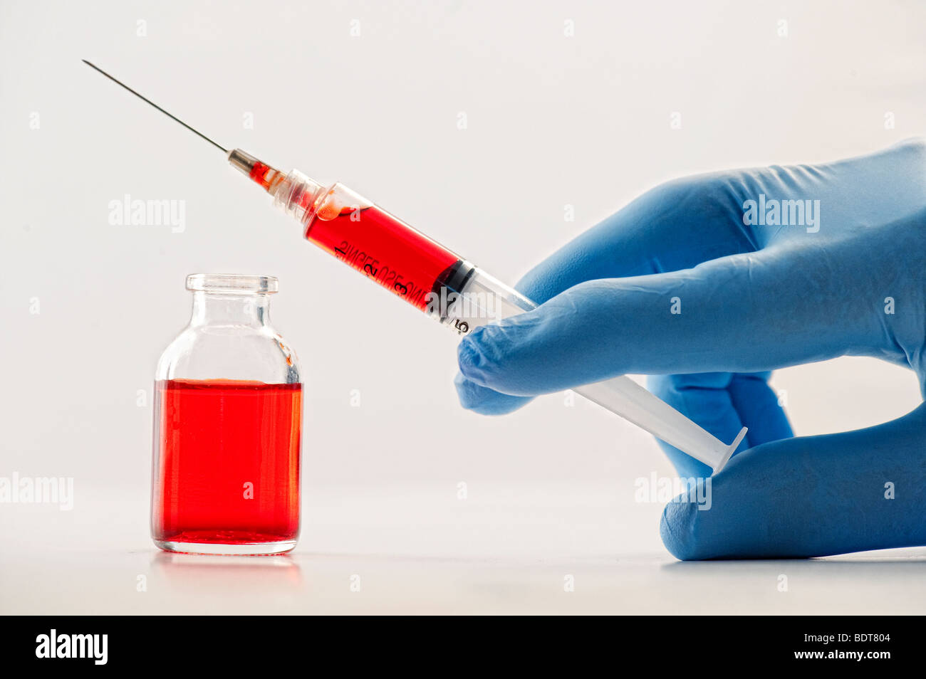 gloved hand holding hypodermic needle and vial Stock Photo