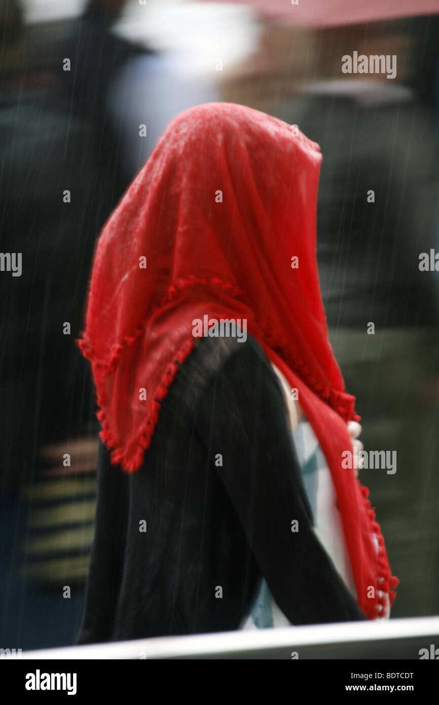 young woman with red scarf covering head in heavy rain in town Stock