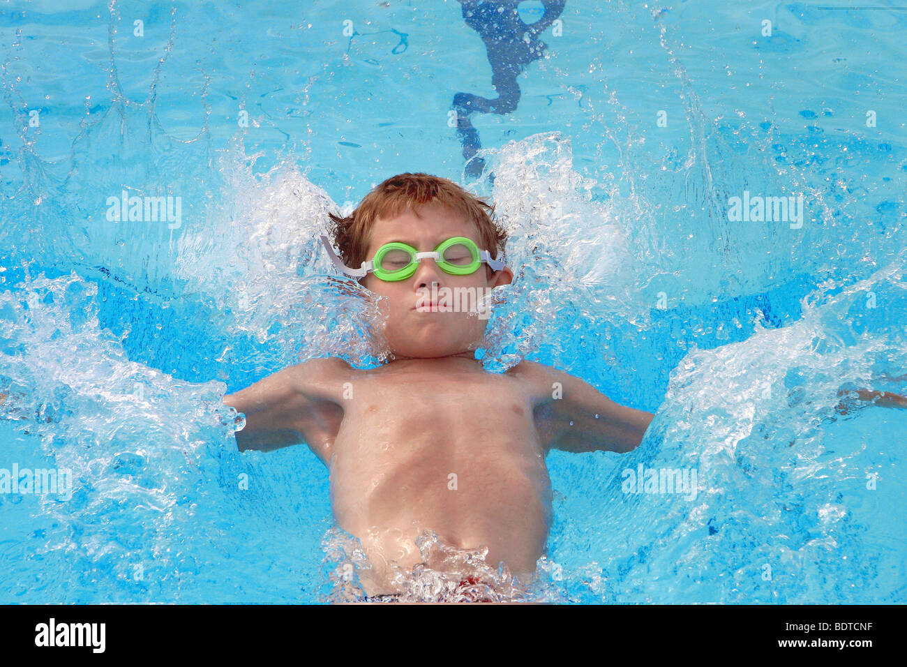 Young boy wearing green goggles in pool doing backstroke at outdoor