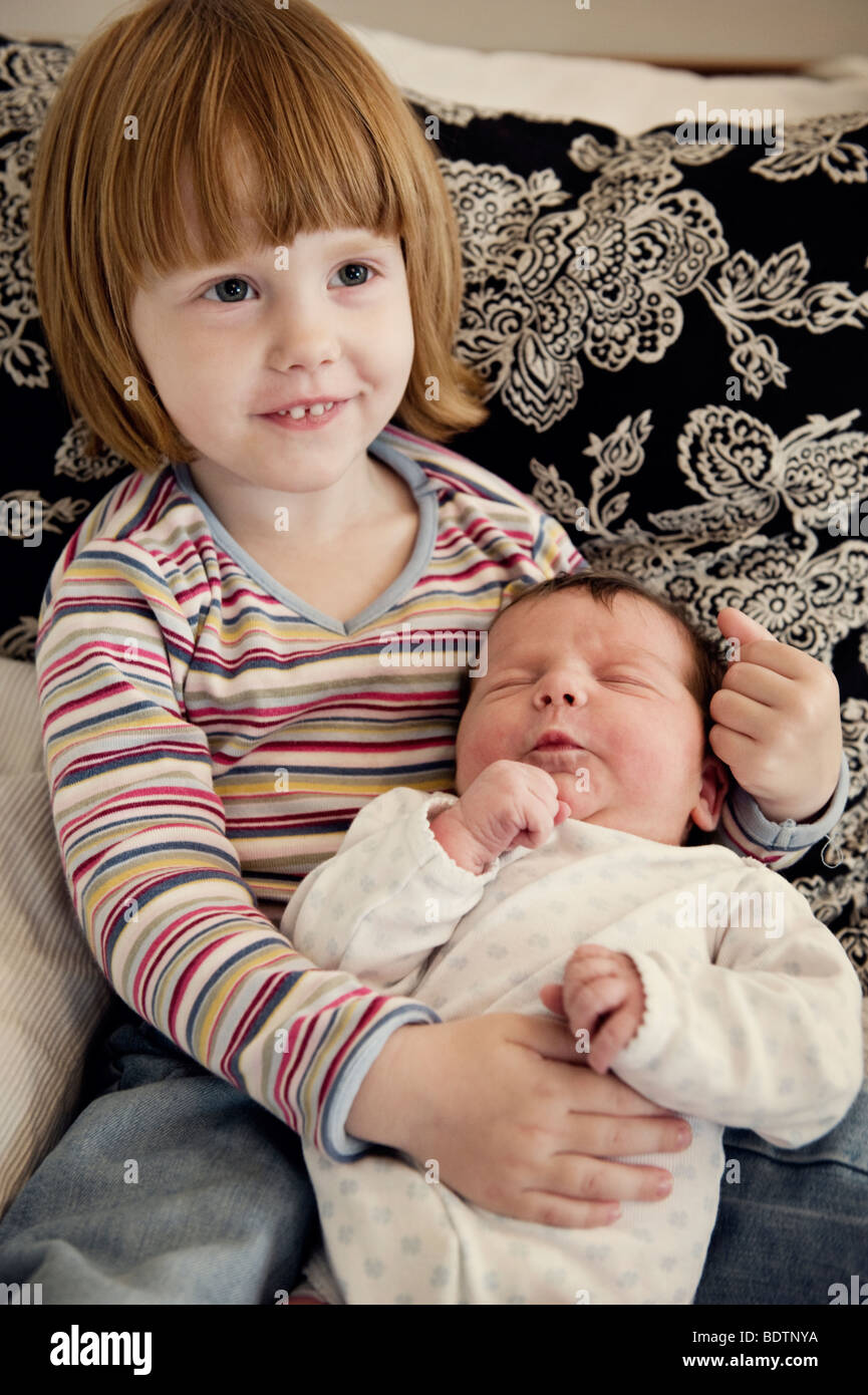 Girl holding her newborn baby sister in her arms Stock Photo