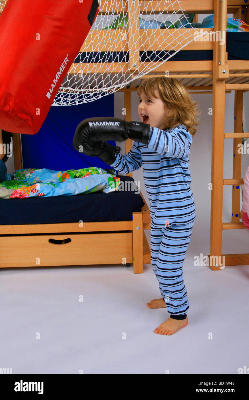 little boy in pyjama training with boxing gloves and the punching bag of a Billi-Bolli loft bed Stock Photo
