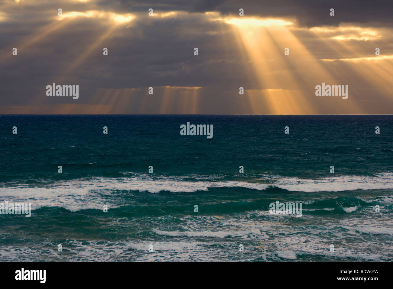 Beams of light break through a dense bank of black clouds over the ocean, Mangawhai Head, Auckland, North Island, New Zealand Stock Photo