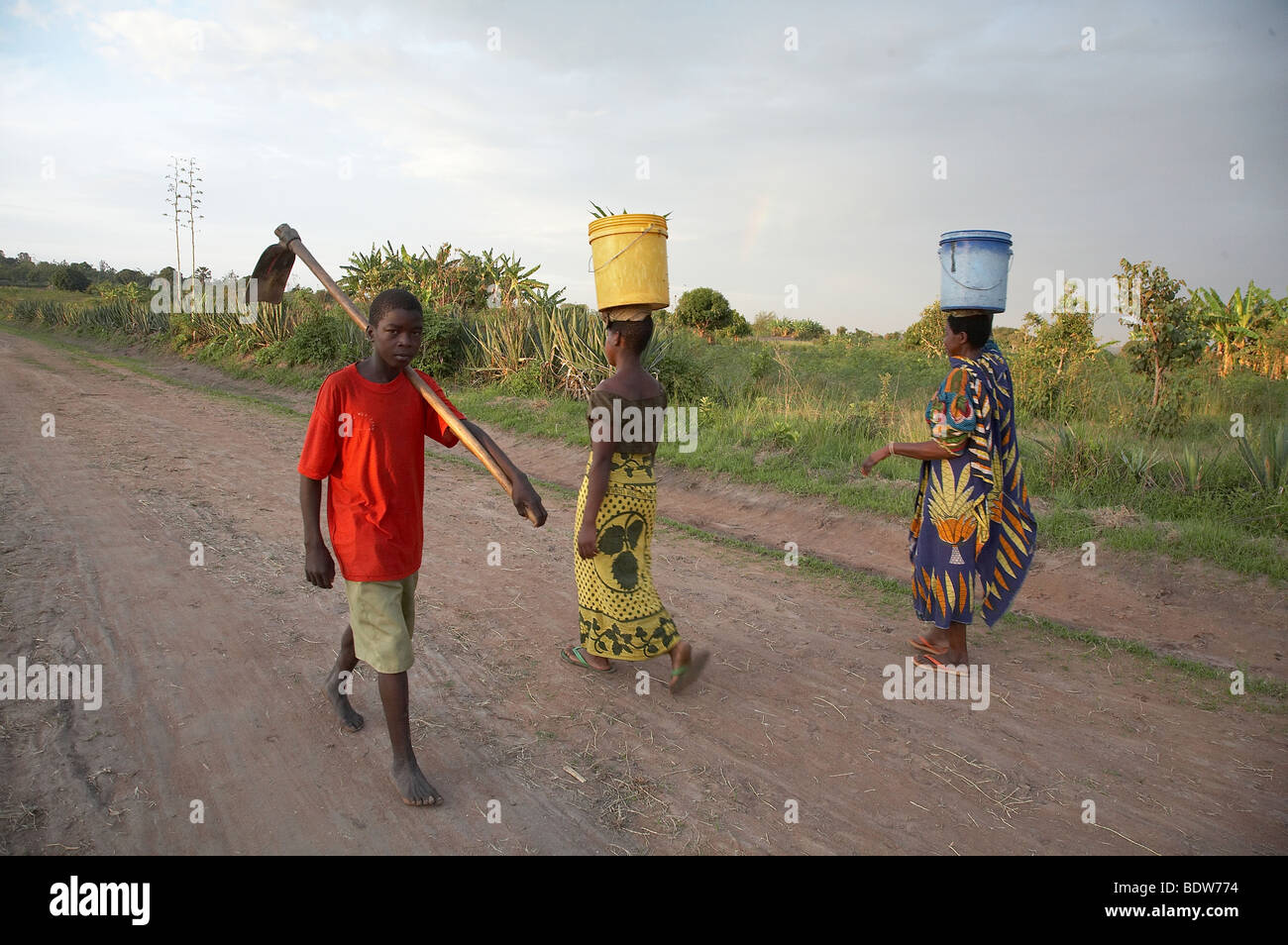 TANZANIA Boy carrying a hoe walking in one direction while women carry buckets of water from a spring in the other. Kalabezo. Stock Photo