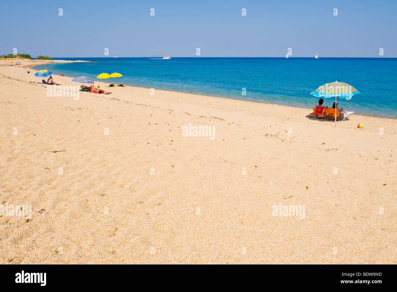 Tourists sunbathe on blue flag beach at Skala on the Greek Mediterranean island of Kefalonia Greece GR Stock Photo
