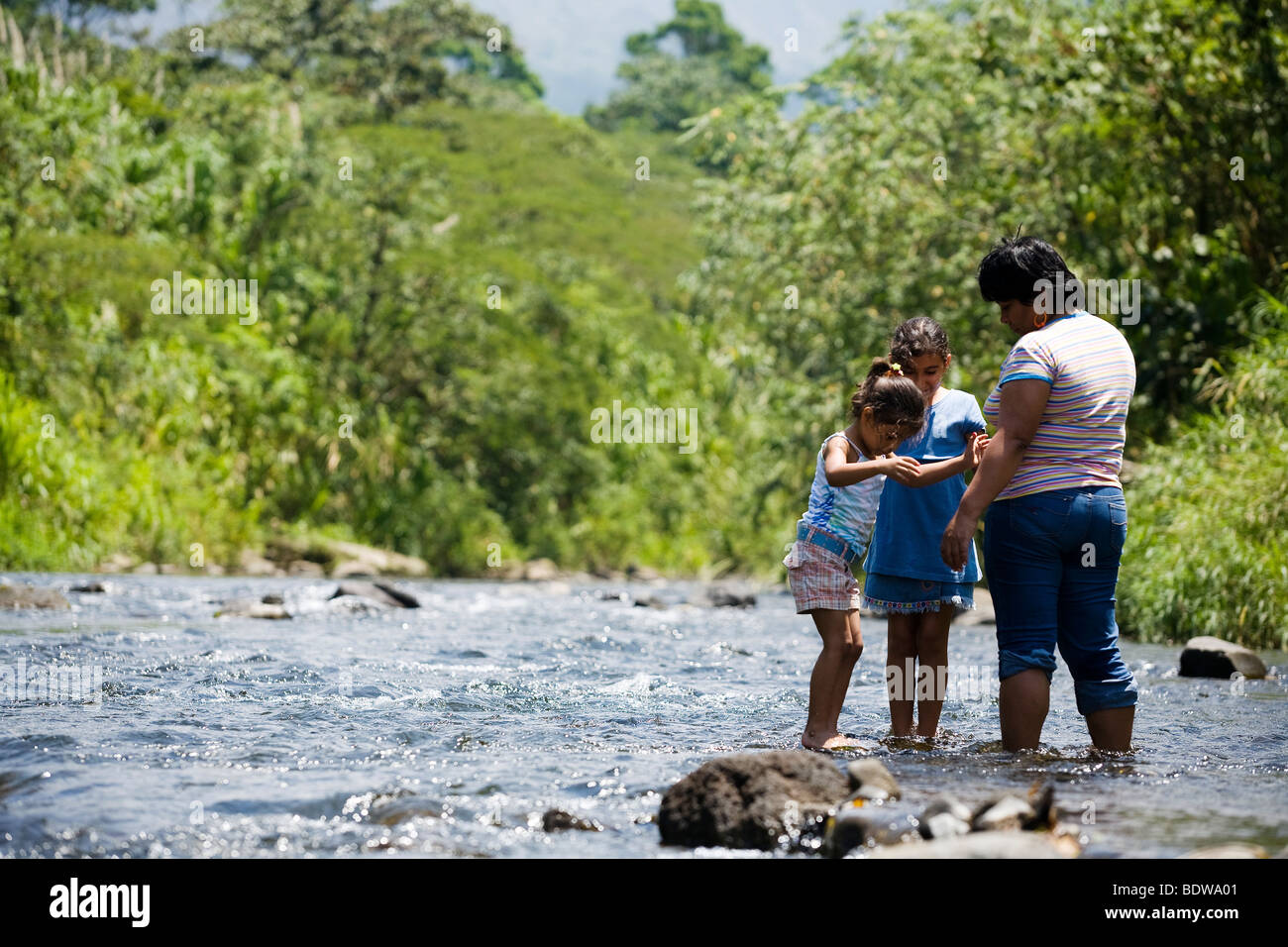 A Costa Rican family stands in a river while looking at Arenal Volcano in Costa Rica close to La Fortuna Stock Photo
