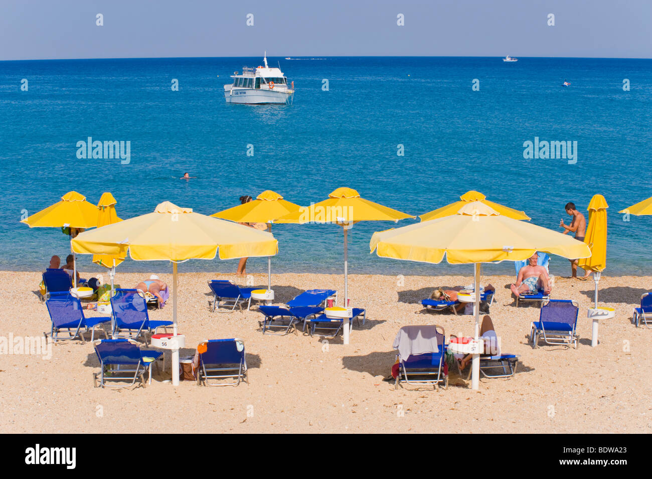 Tourists sunbathe on blue flag beach at Skala on the Greek Mediterranean island of Kefalonia Greece GR Stock Photo