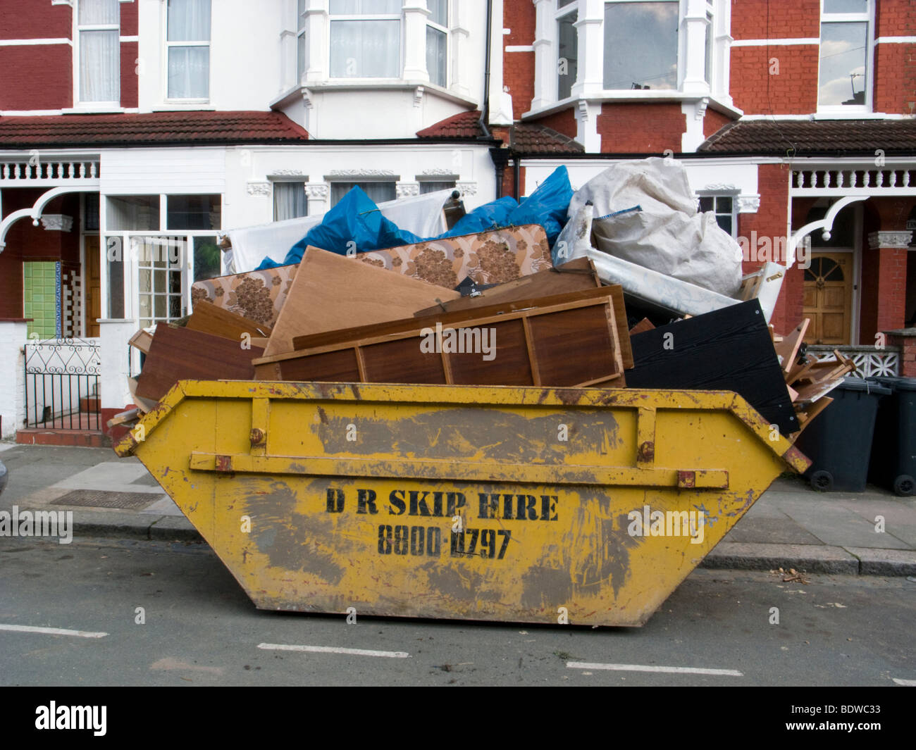 Yellow skip full with household waste on residential street, England, UK Stock Photo