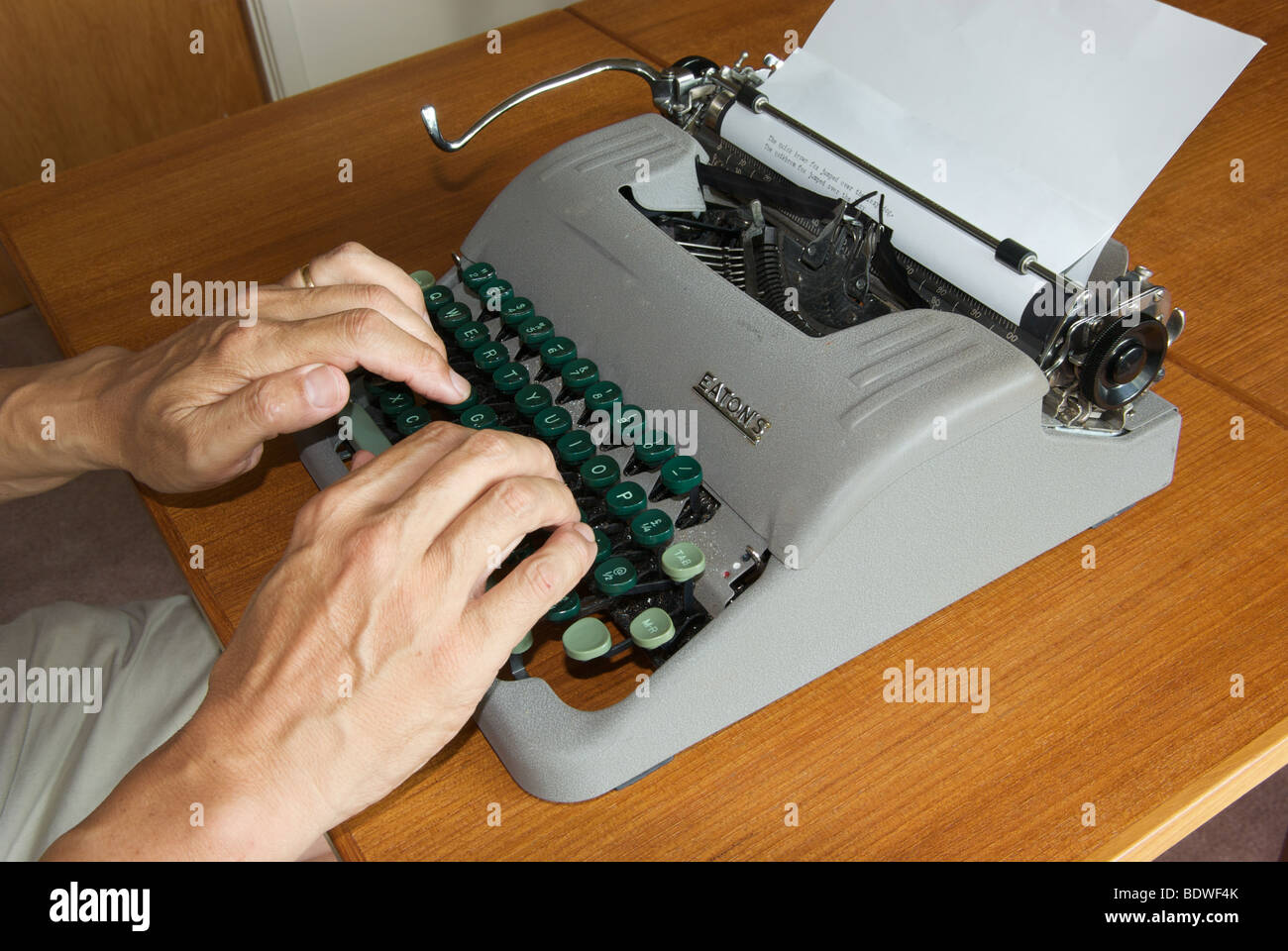 Outdated technology manual portable typewriter fingers typing on keyboard to mechanically activate letter strikes onto paper Stock Photo