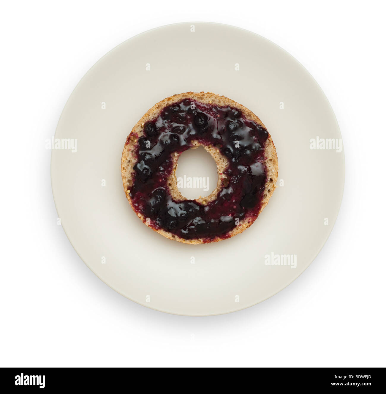 One half of a Whole Grain Bagel with Blueberry Marmalade on a white plate. Isolated on white background. Stock Photo