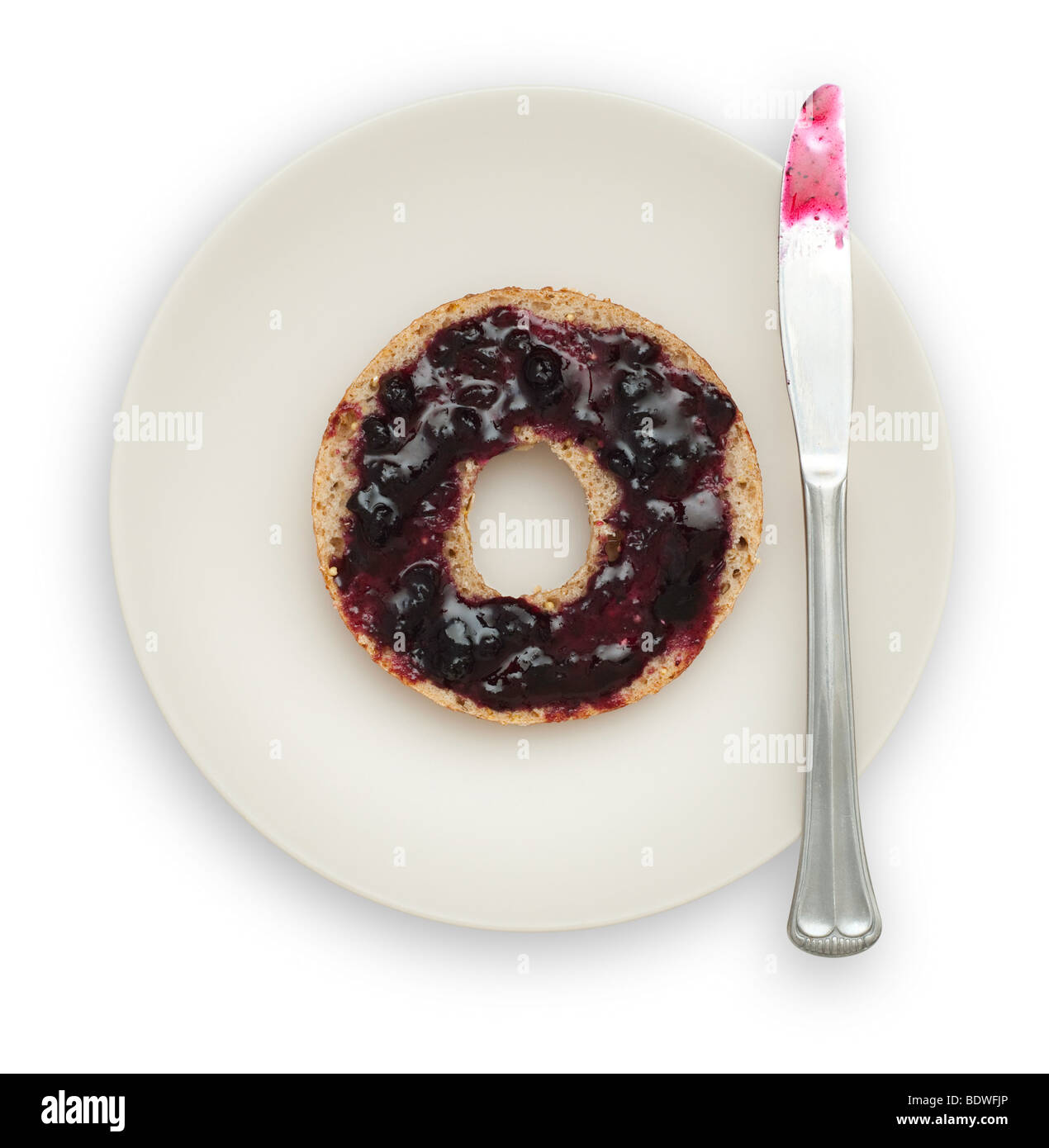 One half of a Whole Grain Bagel with Blueberry Marmalade on a white plate with a knife. Stock Photo