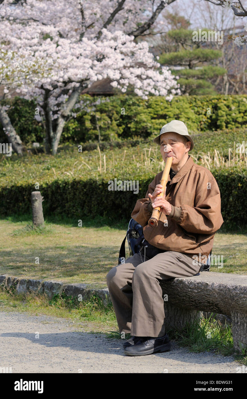 Japanese man playing a shakuhachi, a traditional bamboo flute, outdoors