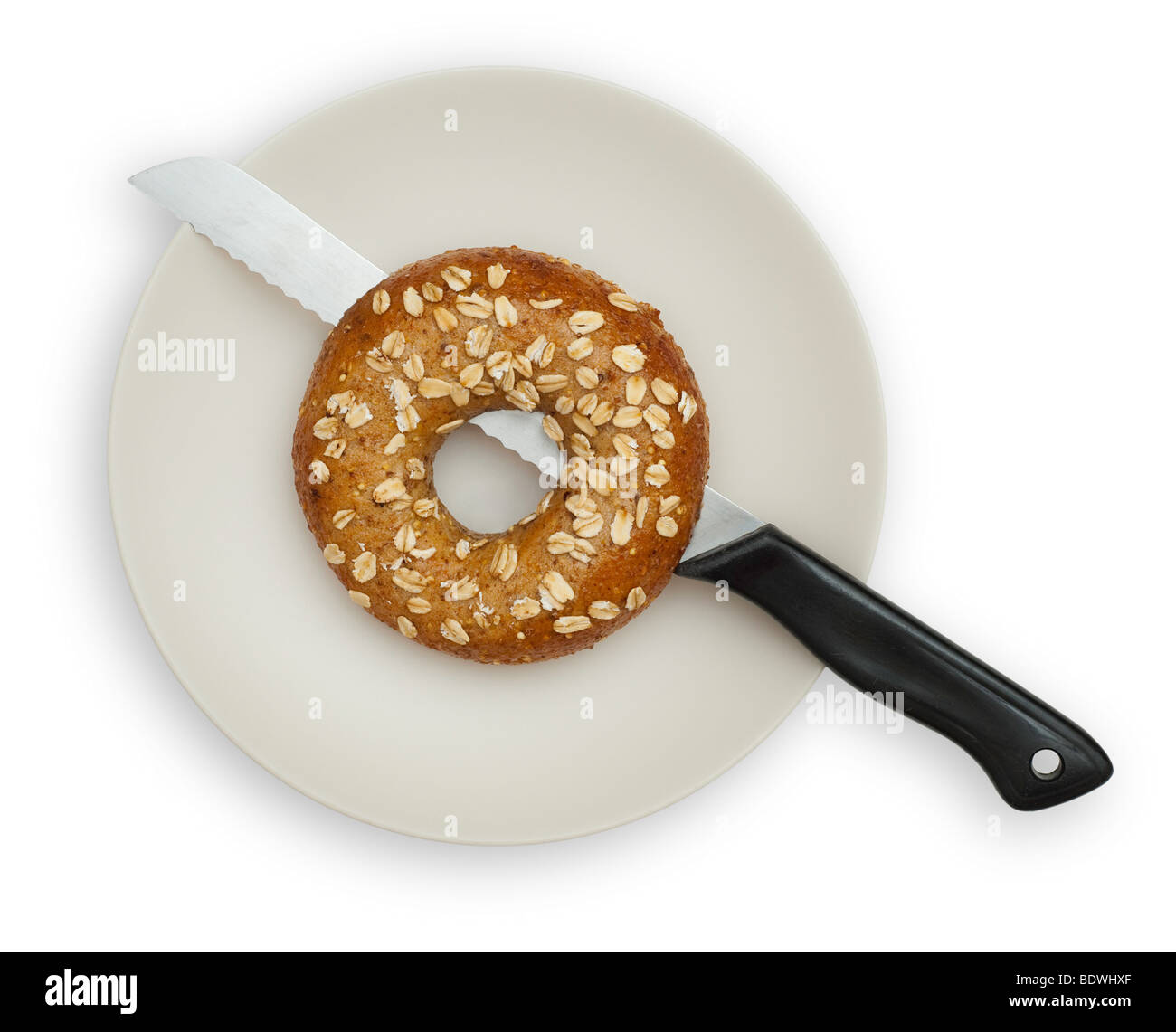 One Whole Grain Bagel on a White plate, isolated on white background. The Bagel is half cut with a knife. Stock Photo