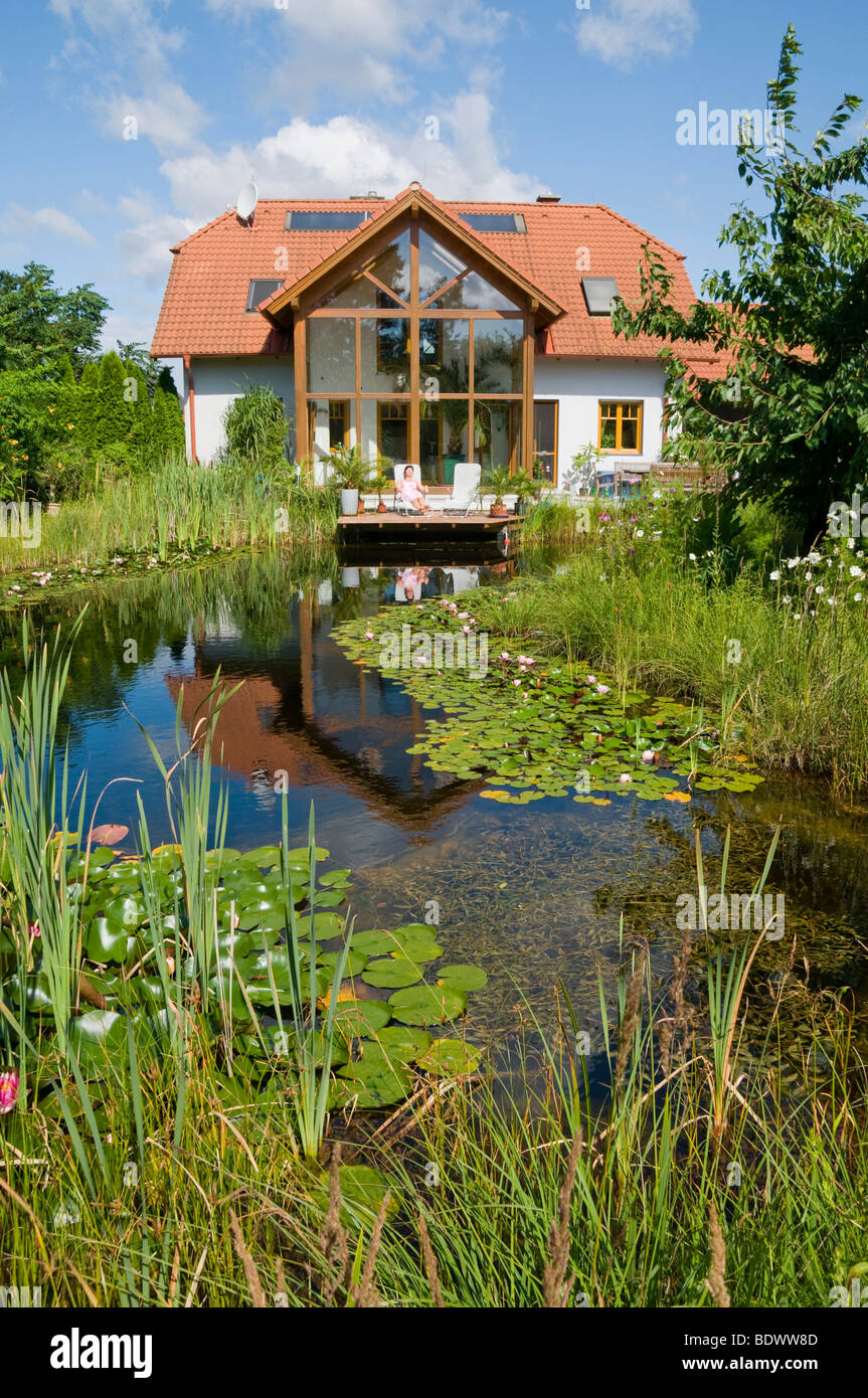 Garden pond with water lilies, in front of house with winter garden, in summer Stock Photo