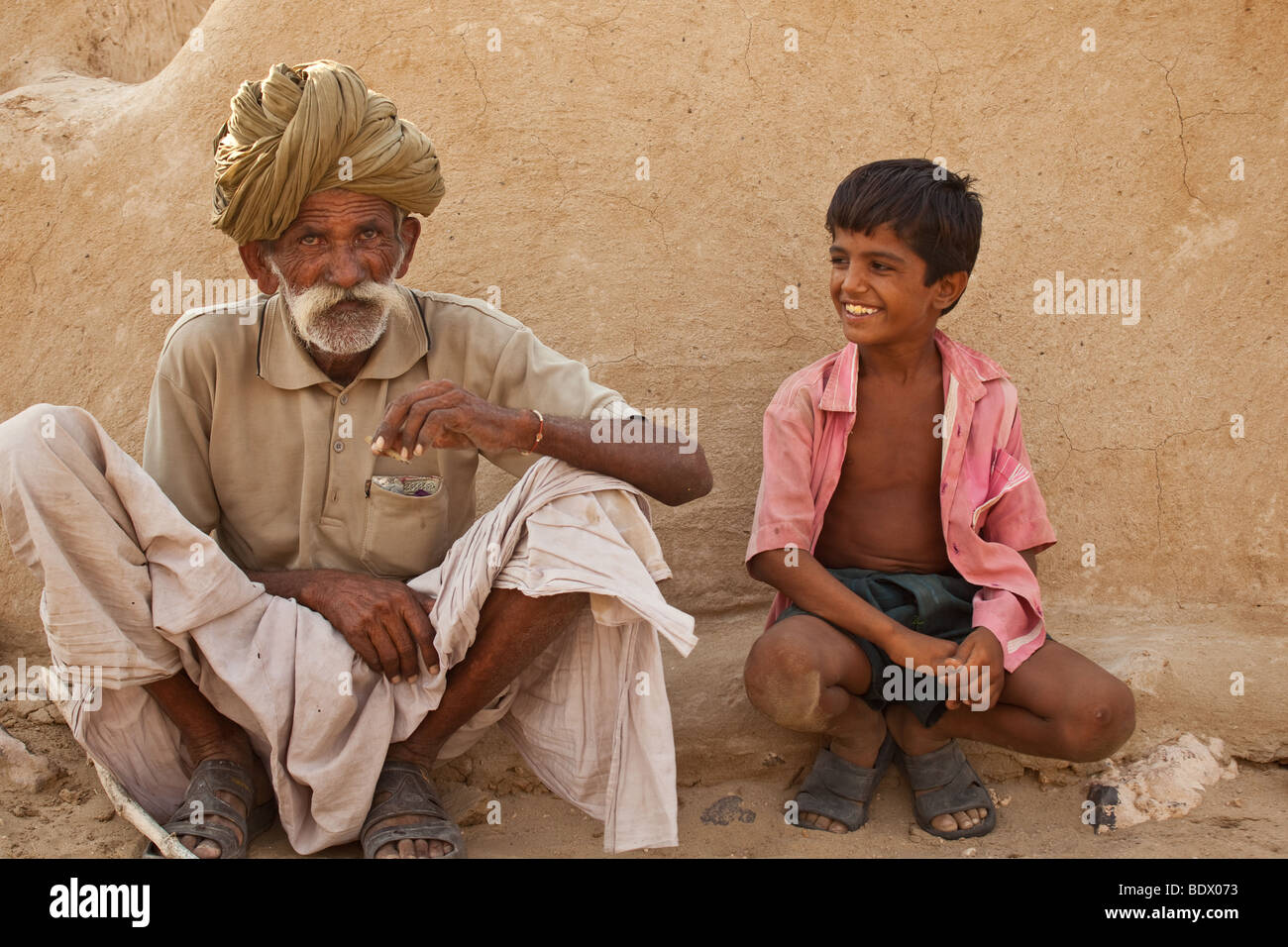 Thar Desert, India  An old Rajput villager smokes a beedi cigarette while a young boy smiles and looks on. Stock Photo