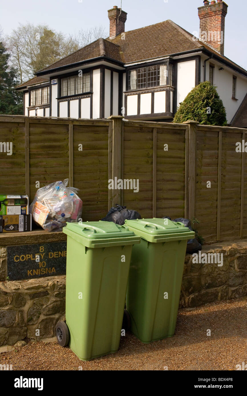 Two green bins and some rubbish for recycling outside a mock Tudor