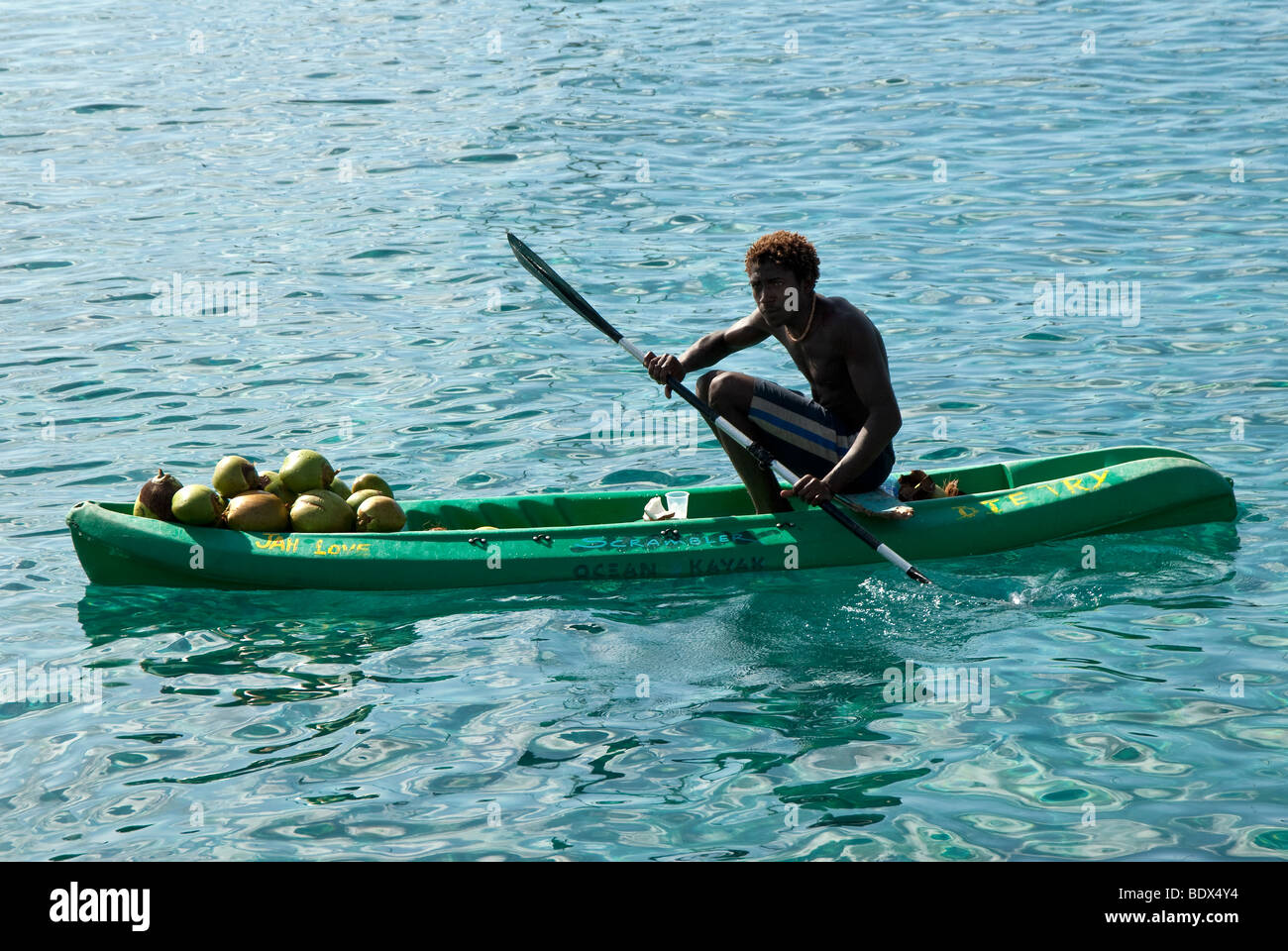 A young Caribbean boy selling coconuts from a kayak near the Caribbean