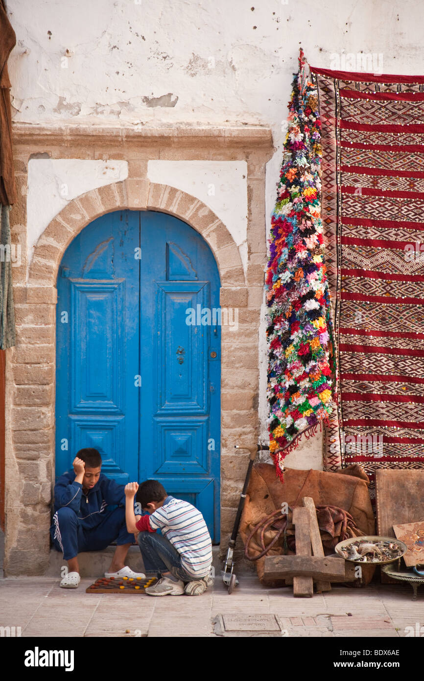 Two boys playing backgammon in front of a blue doorway on the street of Essaouira in Morocco Stock Photo